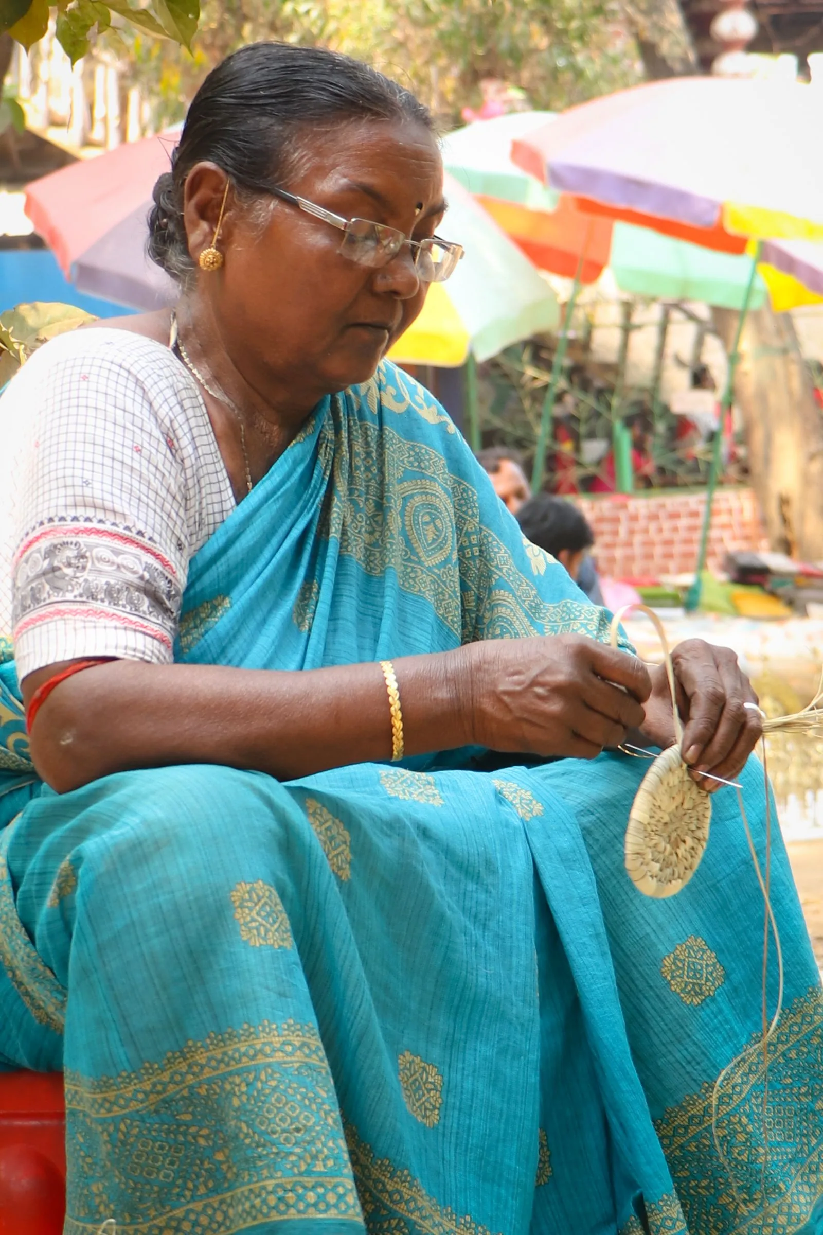Woman weaving a basket at an outdoor market in Santiniketan, West Bengal